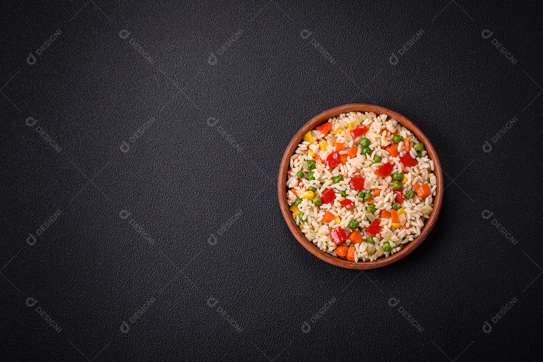 Delicioso arroz cozido branco com legumes, pimentões, cenouras, ervilhas, sal e especiarias sobre um fundo escuro de concreto
