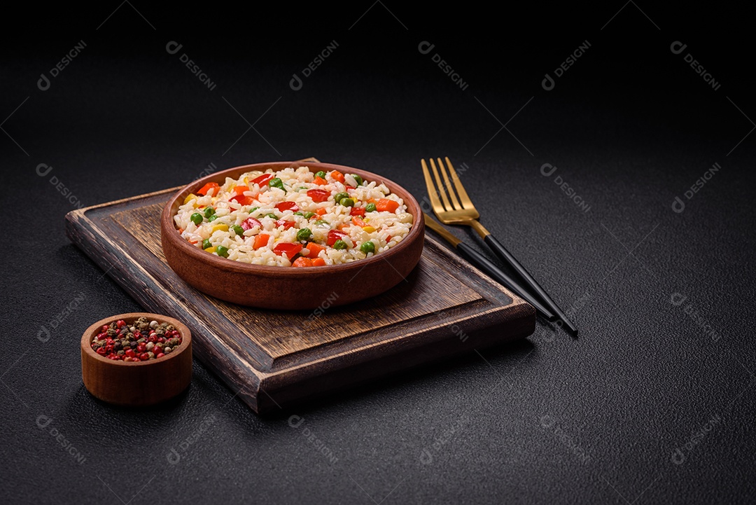 Delicioso arroz cozido branco com legumes, pimentões, cenouras, ervilhas, sal e especiarias sobre um fundo escuro de concreto