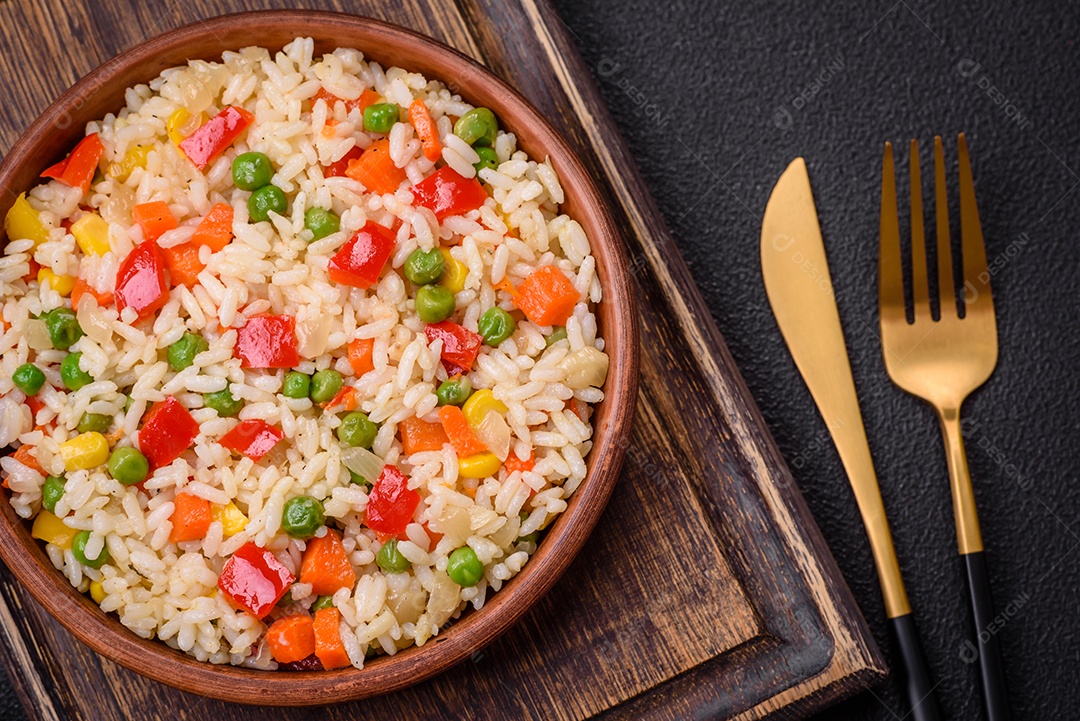 Delicioso arroz cozido branco com legumes, pimentões, cenouras, ervilhas, sal e especiarias sobre um fundo escuro de concreto