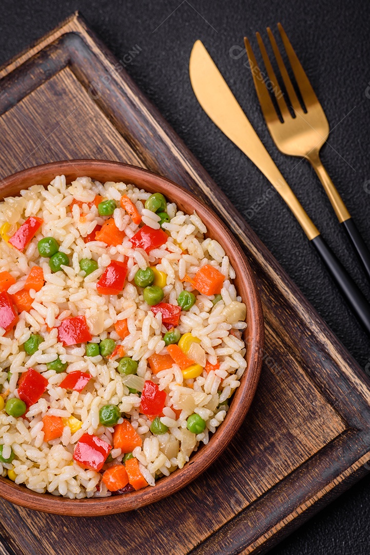 Delicioso arroz cozido branco com legumes, pimentões, cenouras, ervilhas, sal e especiarias sobre um fundo escuro de concreto