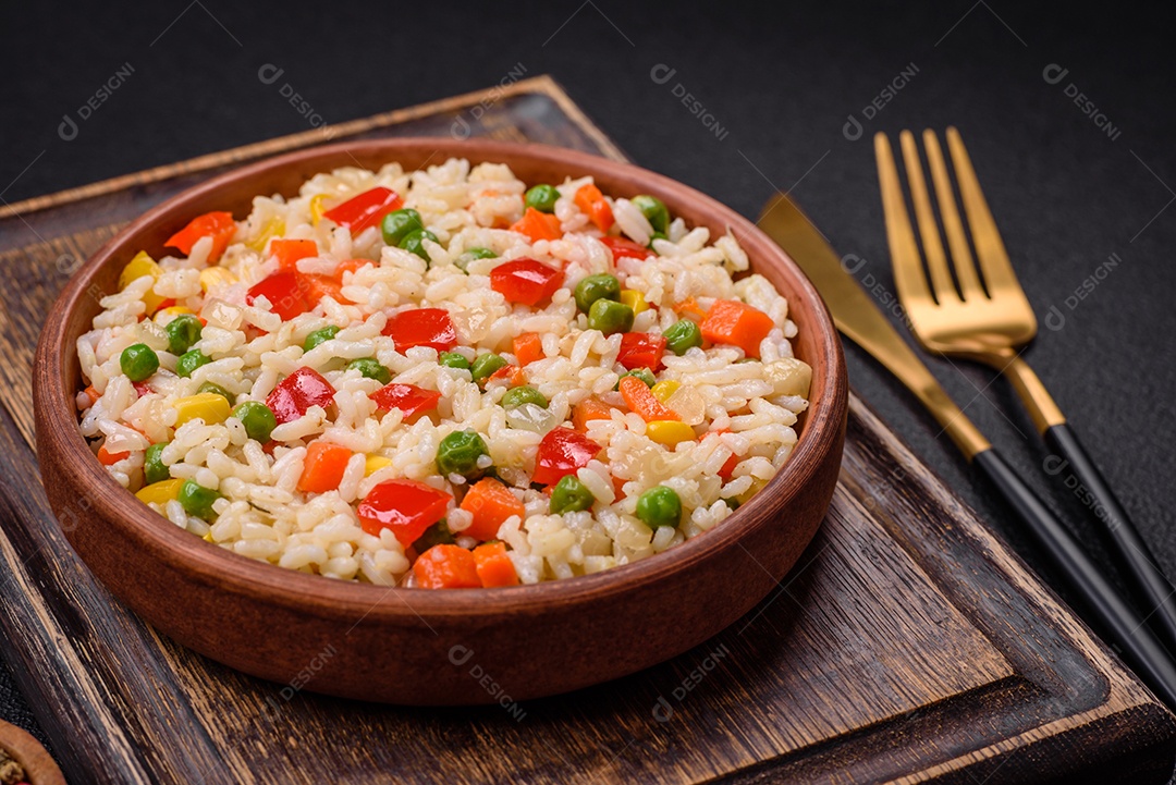 Delicioso arroz cozido branco com legumes, pimentões, cenouras, ervilhas, sal e especiarias sobre um fundo escuro de concreto