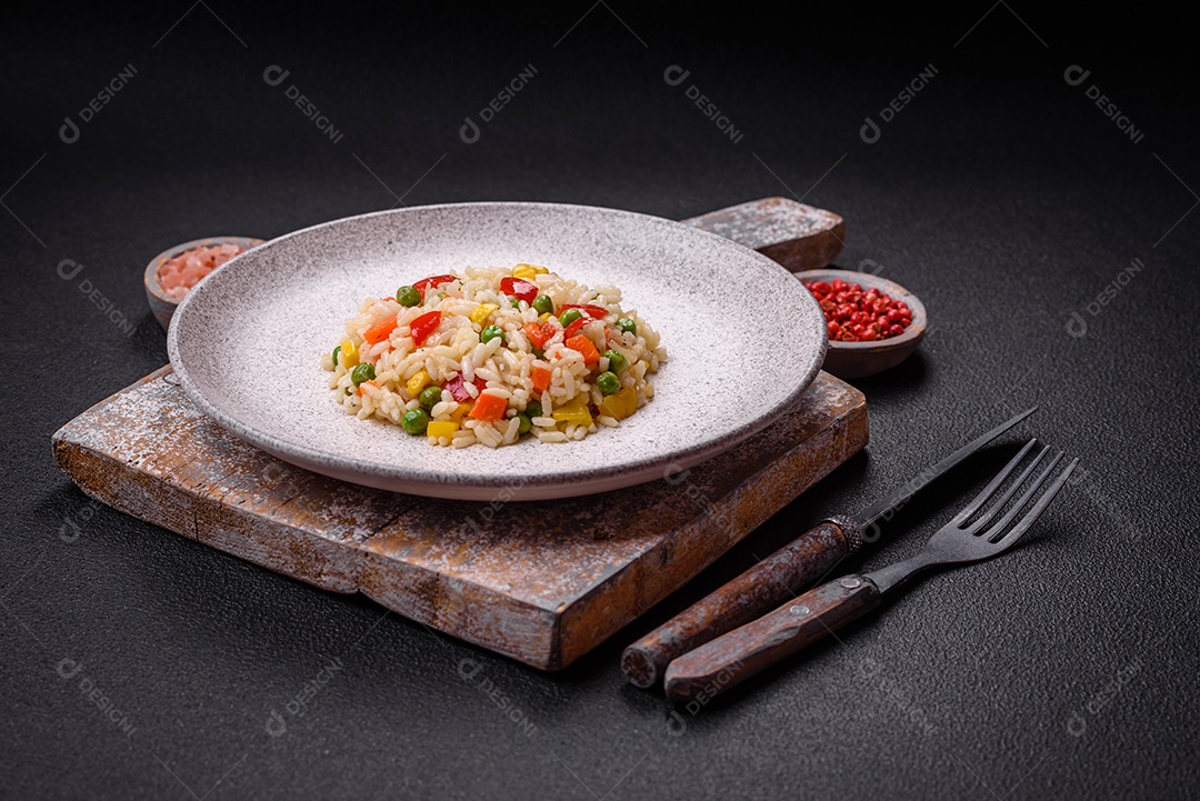 Delicioso arroz cozido branco com legumes, pimentões, cenouras, ervilhas, sal e especiarias sobre um fundo escuro de concreto