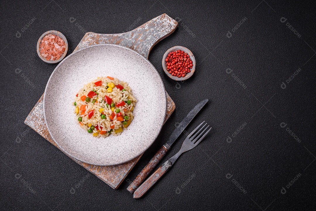 Delicioso arroz cozido branco com legumes, pimentões, cenouras, ervilhas, sal e especiarias sobre um fundo escuro de concreto