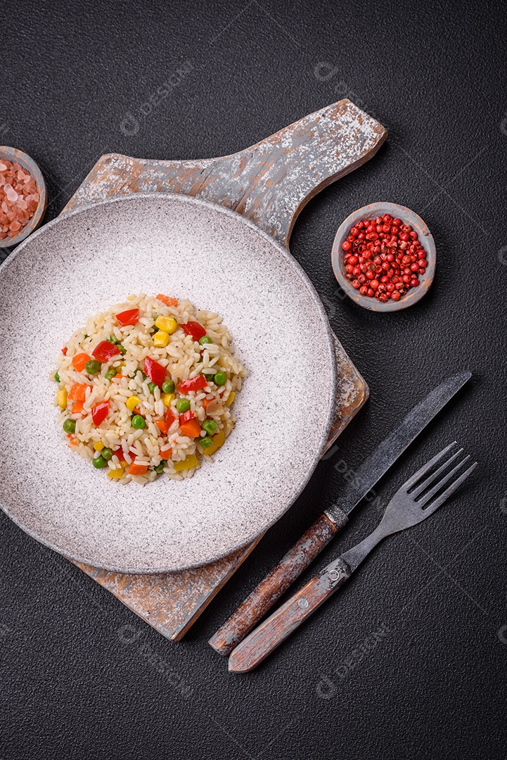 Delicioso arroz cozido branco com legumes, pimentões, cenouras, ervilhas, sal e especiarias sobre um fundo escuro de concreto