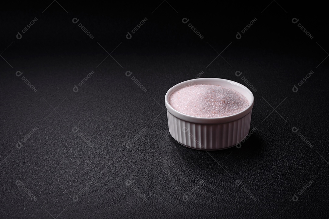 Sal de mesa rosa fino do Himalaia em uma tigela de cerâmica sobre um fundo escuro de concreto