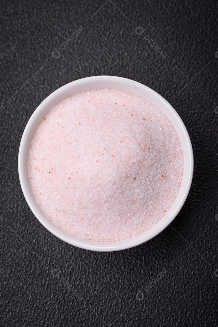 Sal de mesa rosa fino do Himalaia em uma tigela de cerâmica sobre um fundo escuro de concreto