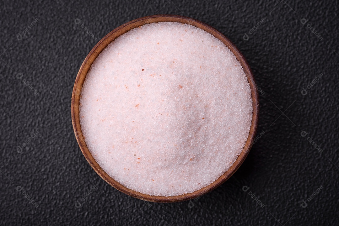 Sal de mesa rosa fino do Himalaia em uma tigela de cerâmica sobre um fundo escuro de concreto