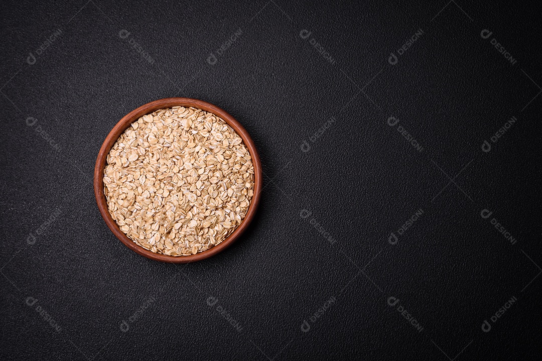 Flocos de aveia crua em uma tigela de cerâmica sobre um fundo escuro de concreto. Preparando um café da manhã delicioso e nutritivo