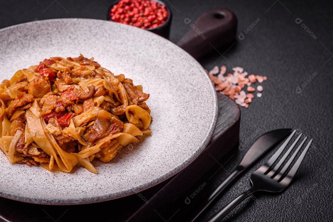 Delicioso prato de udon asiático com legumes, cogumelos, sal e especiarias numa placa cerâmica sobre um fundo escuro de concreto