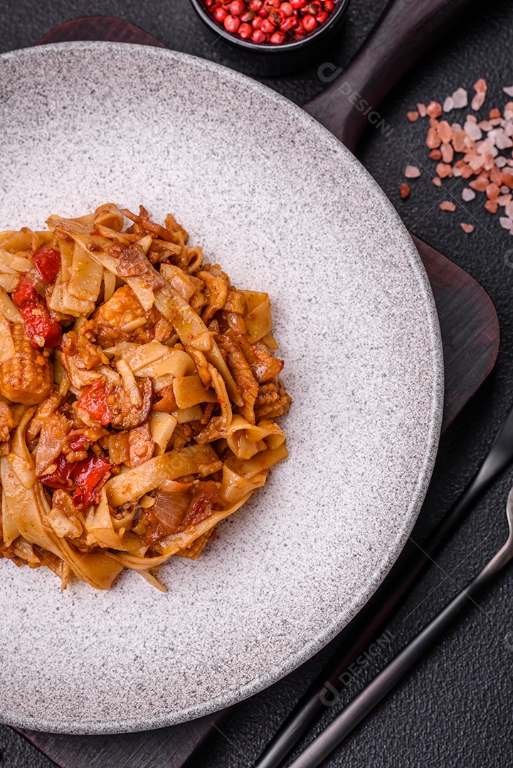 Delicioso prato de udon asiático com legumes, cogumelos, sal e especiarias numa placa cerâmica sobre um fundo escuro de concreto