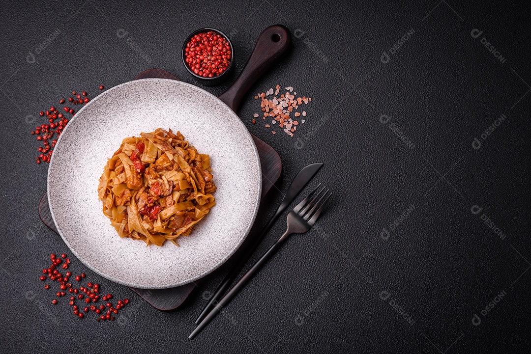 Delicioso prato de udon asiático com legumes, cogumelos, sal e especiarias numa placa cerâmica sobre um fundo escuro de concreto