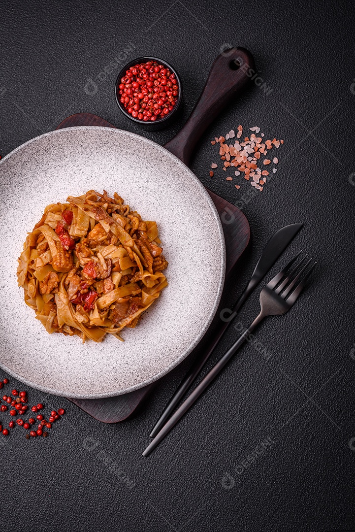 Delicioso prato de udon asiático com legumes, cogumelos, sal e especiarias numa placa cerâmica sobre um fundo escuro de concreto