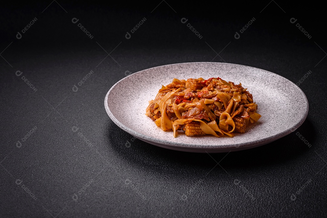Delicioso prato de udon asiático com legumes, cogumelos, sal e especiarias numa placa cerâmica sobre um fundo escuro de concreto