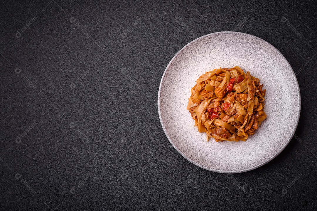 Delicioso prato de udon asiático com legumes, cogumelos, sal e especiarias numa placa cerâmica sobre um fundo escuro de concreto