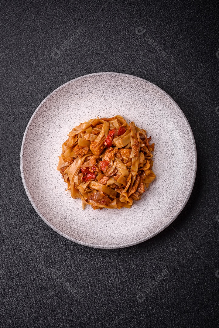 Delicioso prato de udon asiático com legumes, cogumelos, sal e especiarias numa placa cerâmica sobre um fundo escuro de concreto