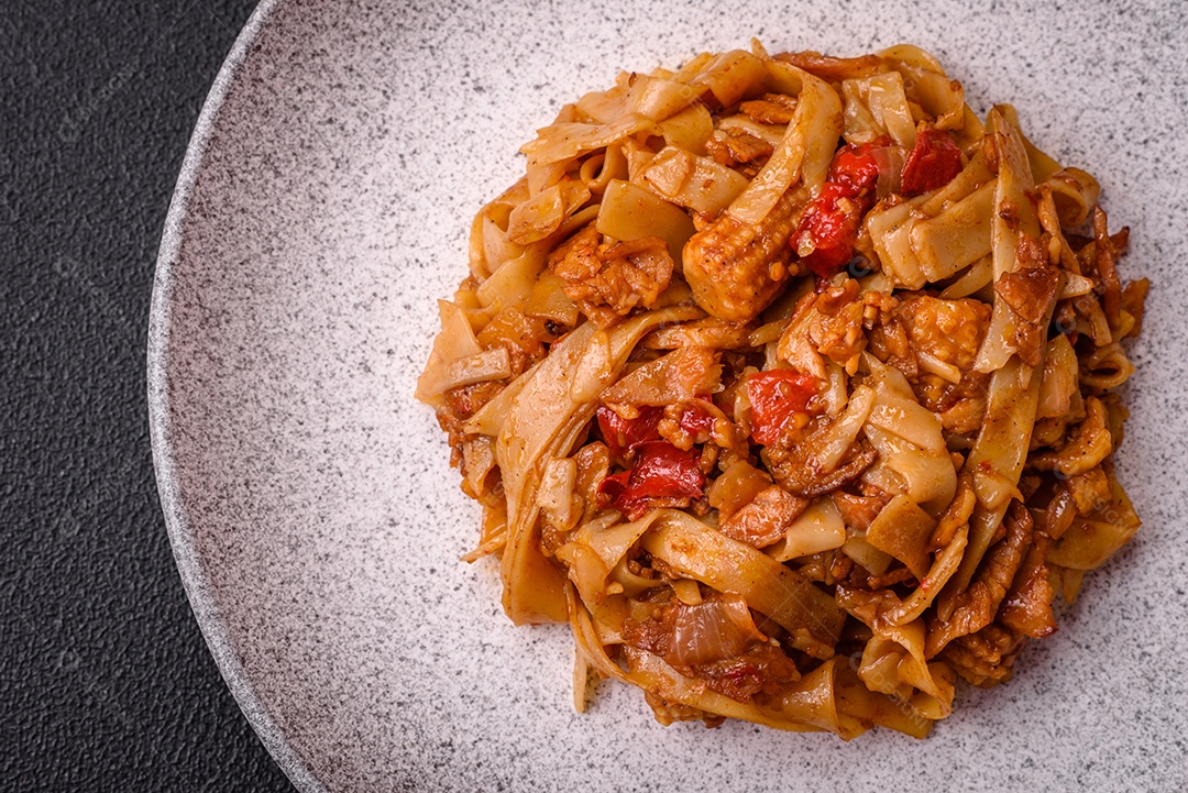 Delicioso prato de udon asiático com legumes, cogumelos, sal e especiarias numa placa cerâmica sobre um fundo escuro de concreto
