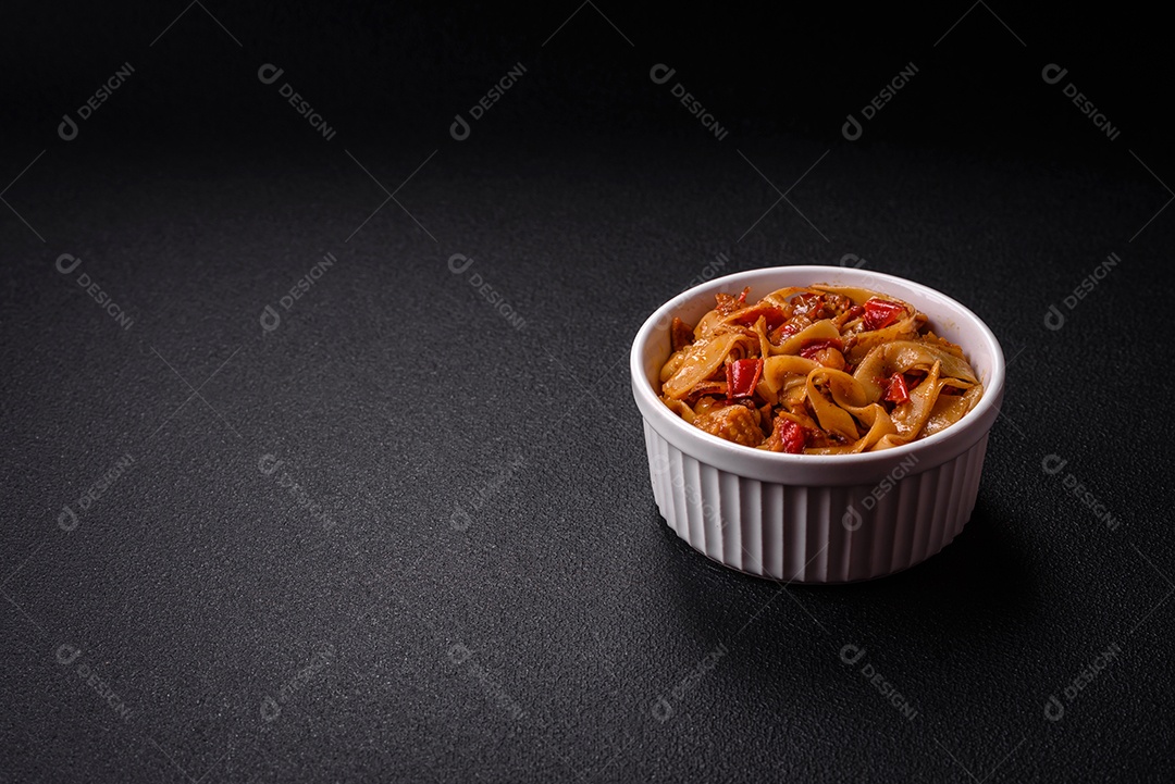 Delicioso prato de udon asiático com legumes, cogumelos, sal e especiarias numa placa cerâmica sobre um fundo escuro de concreto