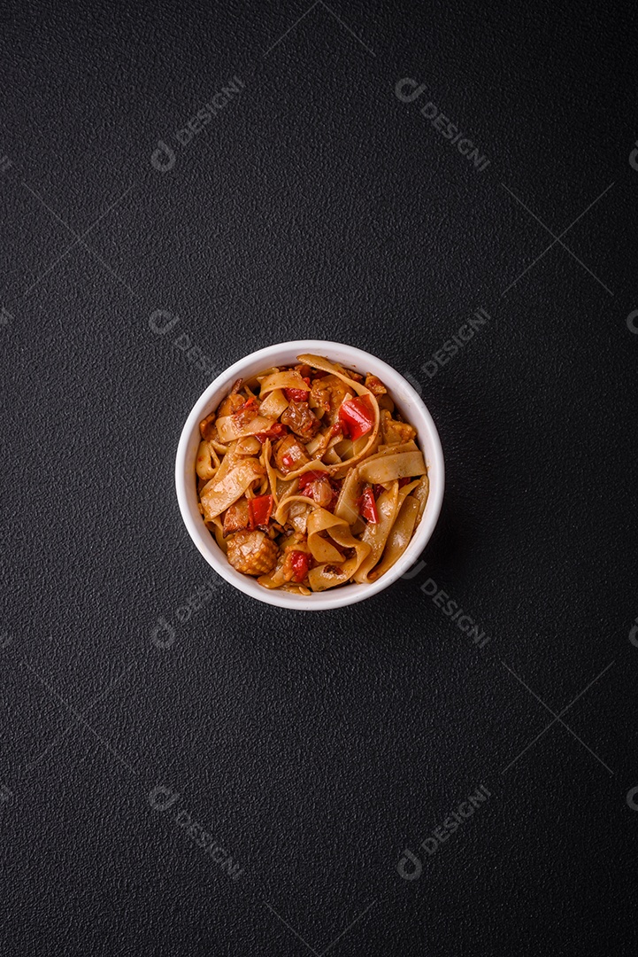 Delicioso prato de udon asiático com legumes, cogumelos, sal e especiarias numa placa cerâmica sobre um fundo escuro de concreto