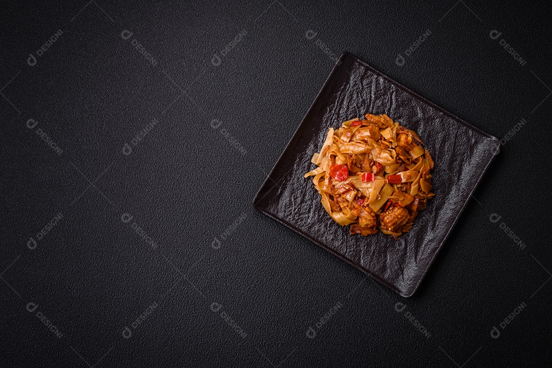 Delicioso prato de udon asiático com legumes, cogumelos, sal e especiarias numa placa cerâmica sobre um fundo escuro de concreto