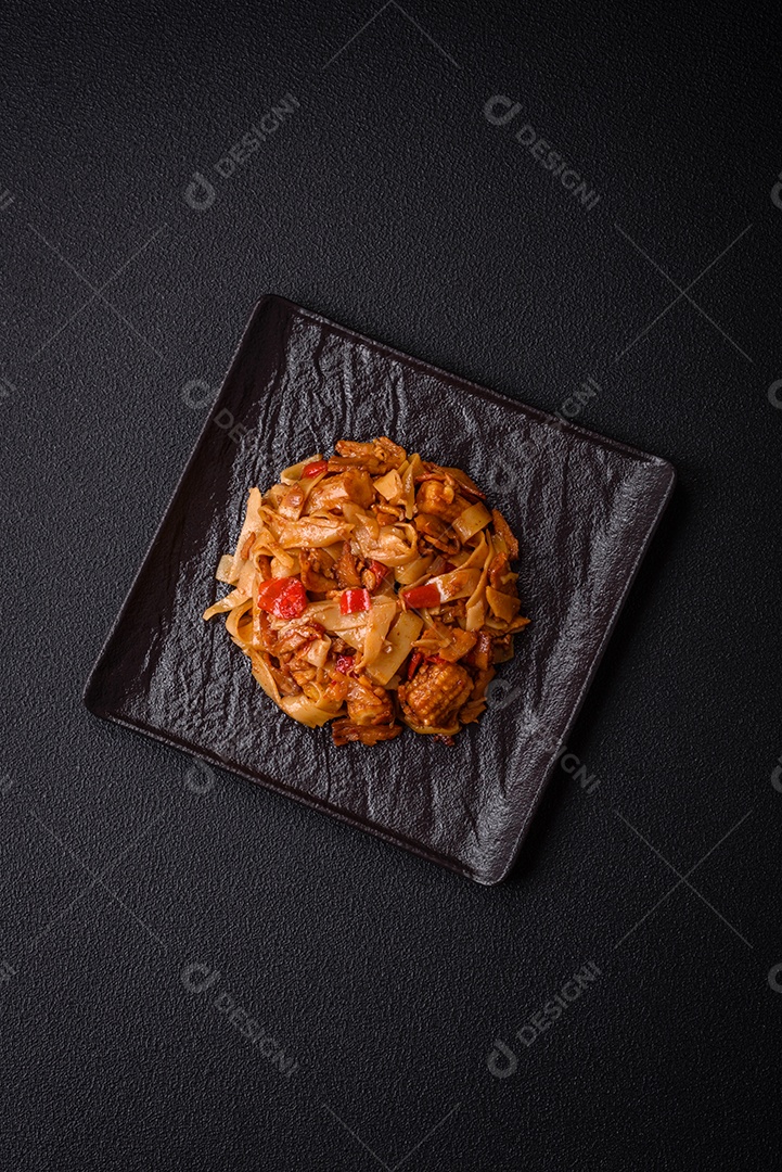 Delicioso prato de udon asiático com legumes, cogumelos, sal e especiarias numa placa cerâmica sobre um fundo escuro de concreto