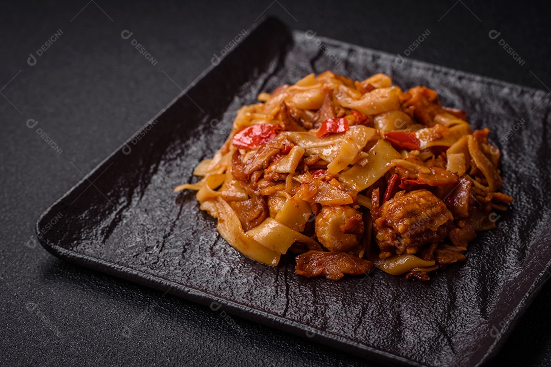 Delicioso prato de udon asiático com legumes, cogumelos, sal e especiarias numa placa cerâmica sobre um fundo escuro de concreto