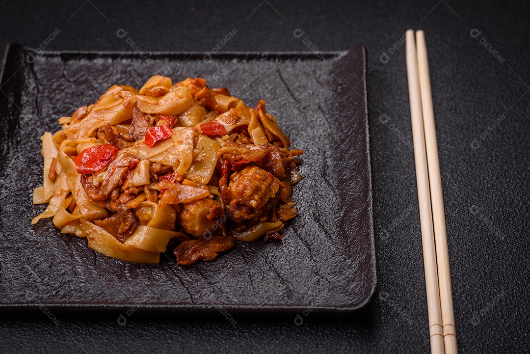 Delicioso prato de udon asiático com legumes, cogumelos, sal e especiarias numa placa cerâmica sobre um fundo escuro de concreto