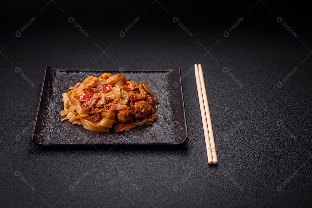 Delicioso prato de udon asiático com legumes, cogumelos, sal e especiarias numa placa cerâmica sobre um fundo escuro de concreto