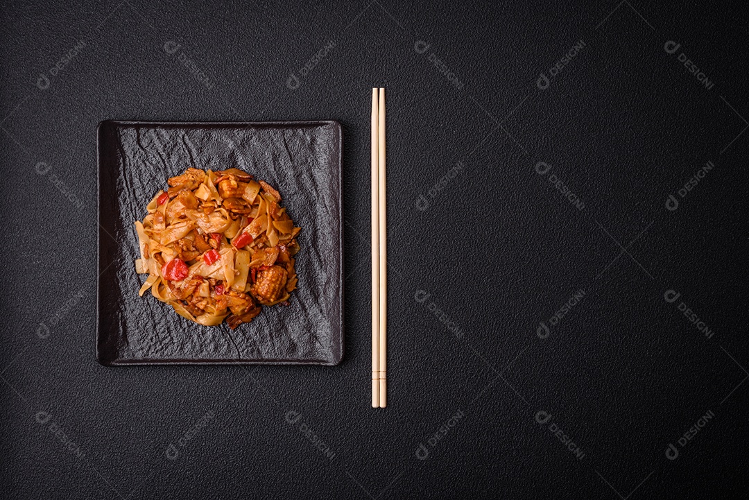 Delicioso prato de udon asiático com legumes, cogumelos, sal e especiarias numa placa cerâmica sobre um fundo escuro de concreto