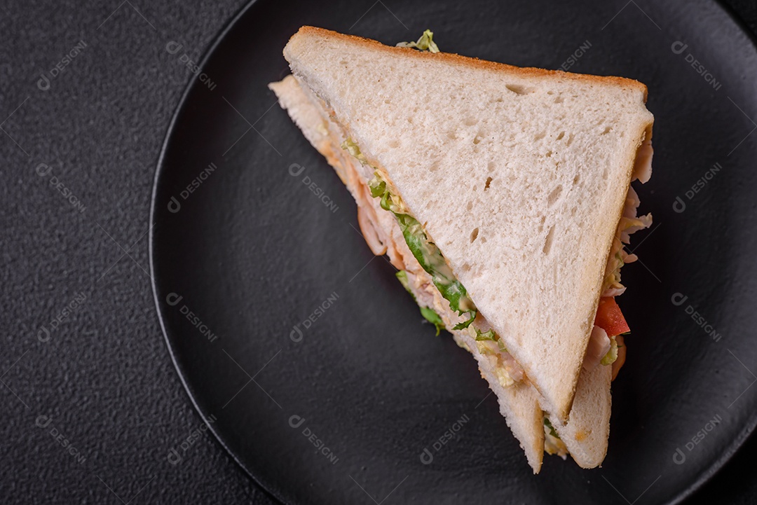 Delicioso sanduíche nutritivo com pão torrado, presunto, tomate, queijo e molho sobre um fundo escuro de concreto