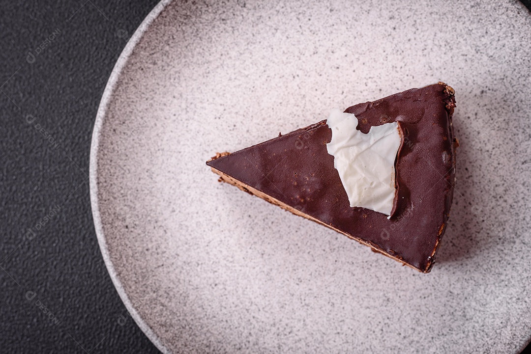 Pedaço de delicioso bolo de chocolate doce com pão de ló e creme sobre um fundo escuro de concreto