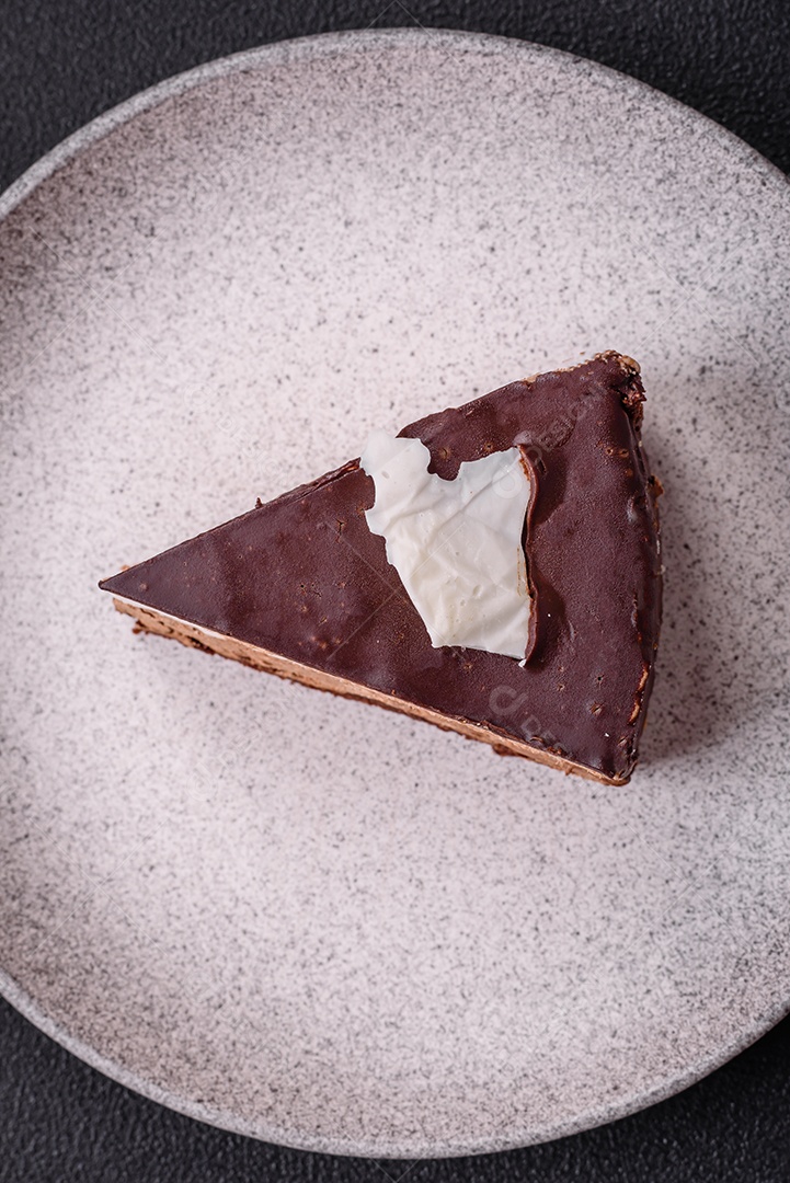 Pedaço de delicioso bolo de chocolate doce com pão de ló e creme sobre um fundo escuro de concreto