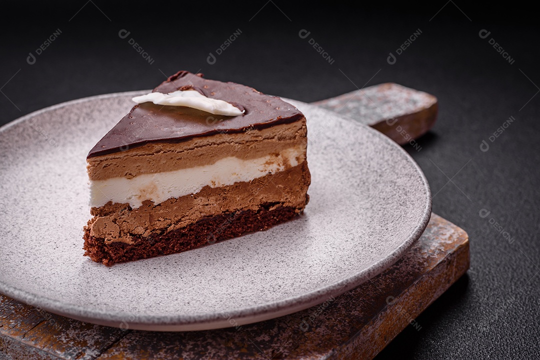 Pedaço de delicioso bolo de chocolate doce com pão de ló e creme sobre um fundo escuro de concreto