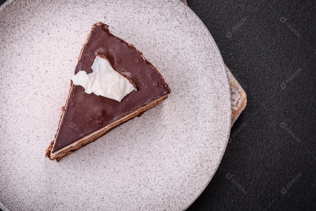 Pedaço de delicioso bolo de chocolate doce com pão de ló e creme sobre um fundo escuro de concreto