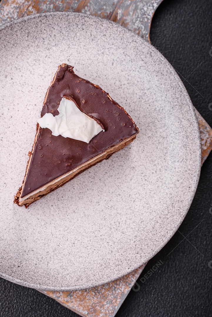 Pedaço de delicioso bolo de chocolate doce com pão de ló e creme sobre um fundo escuro de concreto