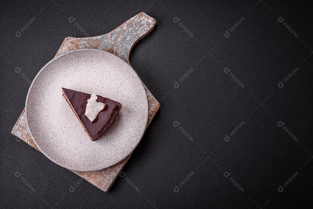 Pedaço de delicioso bolo de chocolate doce com pão de ló e creme sobre um fundo escuro de concreto