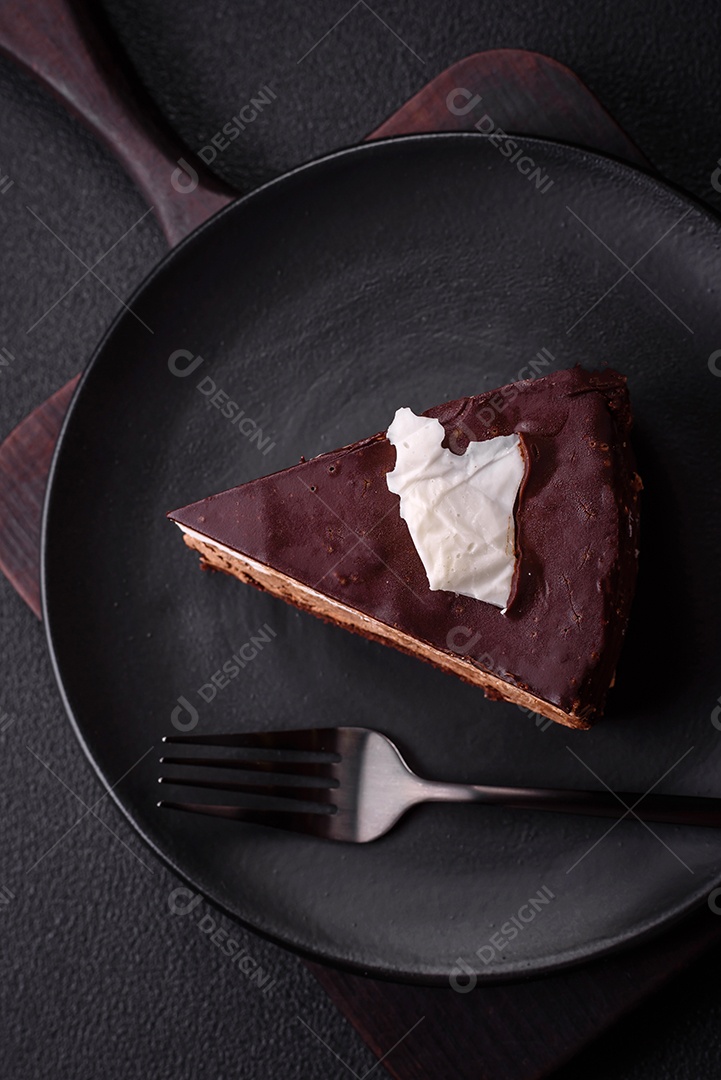 Pedaço de delicioso bolo de chocolate doce com pão de ló e creme sobre um fundo escuro de concreto