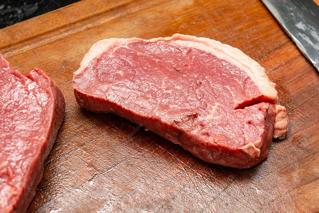 Bifes crus sobre tábua de madeira.
