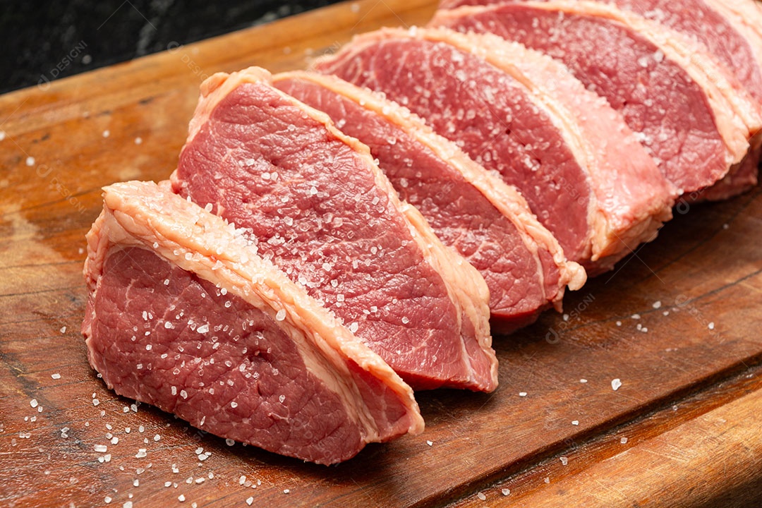 Bifes crus temperado com sal sobre tábua de madeira.