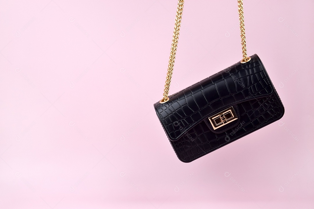 Bolsa feminina negra com alças douradas sobre fundo rosa