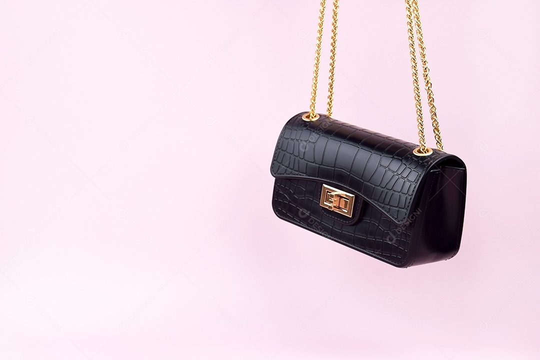 Bolsa feminina negra com alças douradas sobre fundo rosa