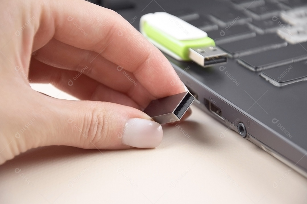 Mão segurando cartão de memória USB branco verde no teclado de um laptop aberto