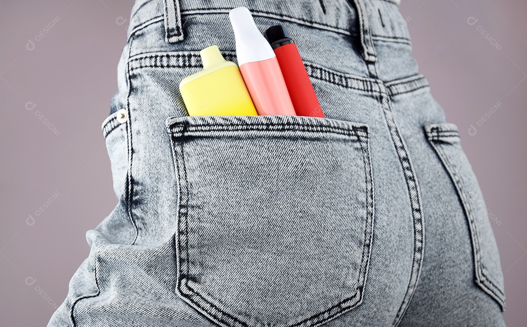 Mulher com cigarros eletrônicos em bolso de jeans sobre fundo claro