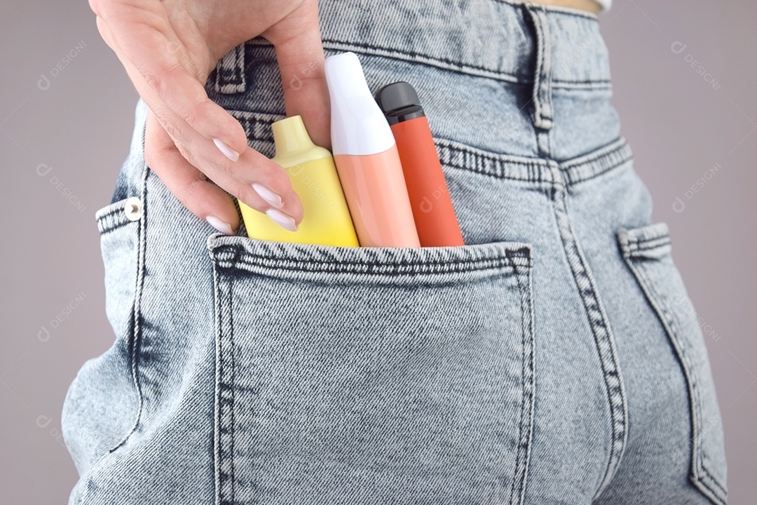 Mulher com cigarros eletrônicos em bolso de jeans sobre fundo claro
