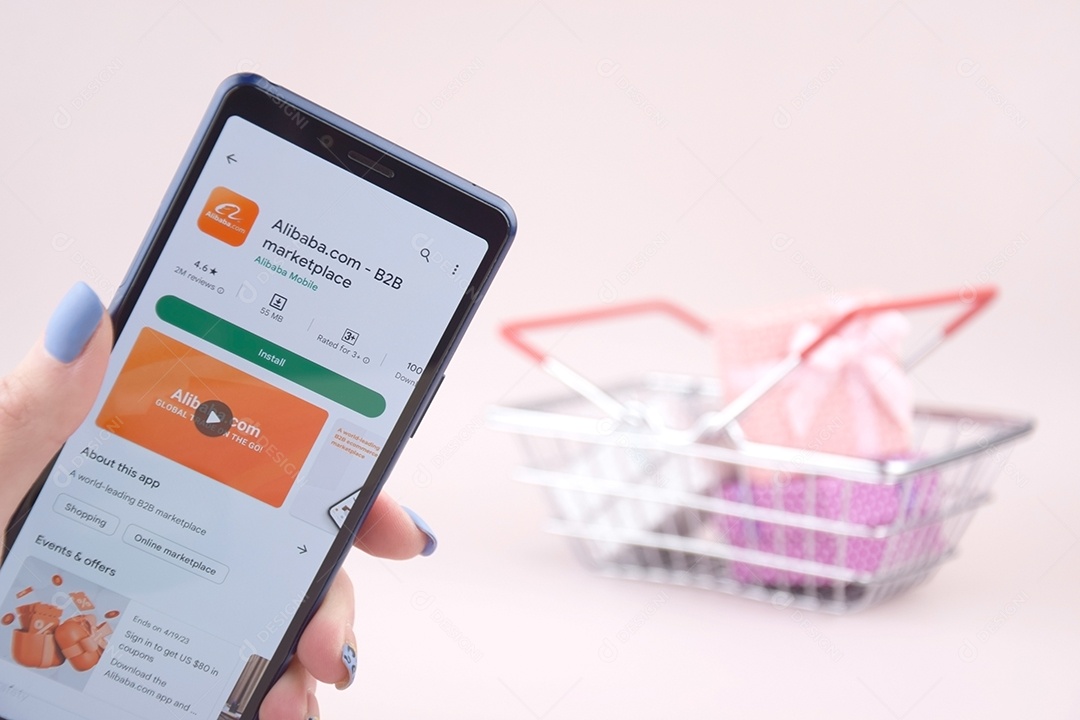 Cesta de compra e celular na mão com aplicativo Alibaba sobre fundo rosa