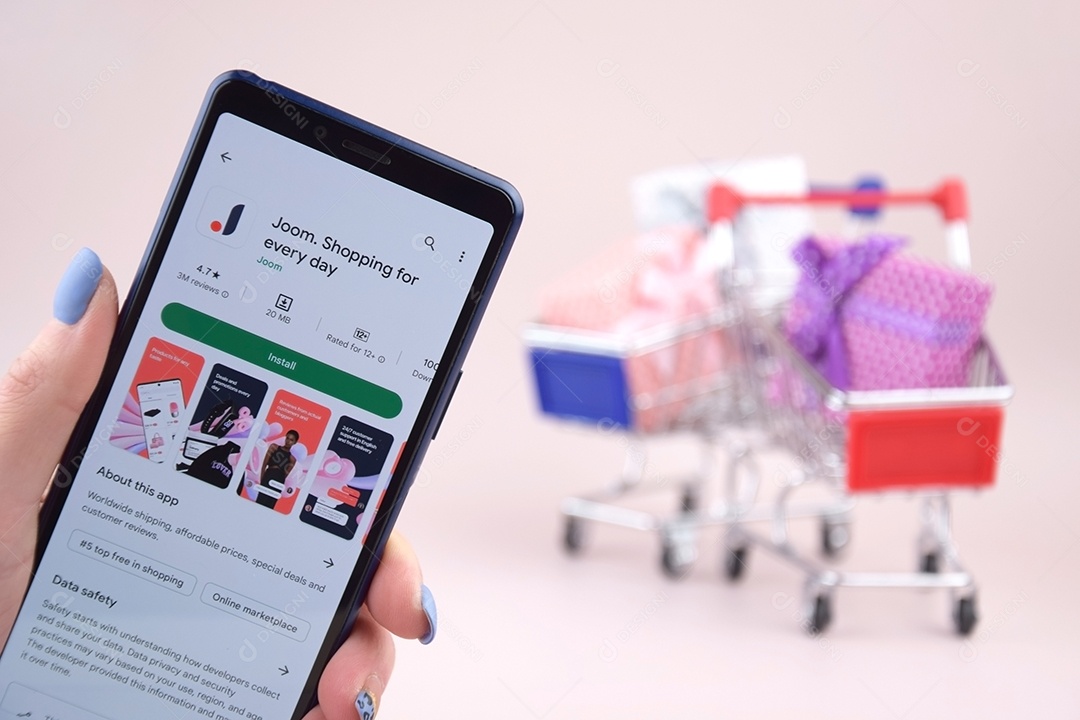 Carrinho de compras com um smartphone abriu o logotipo do Joom na tela em um fundo rosa