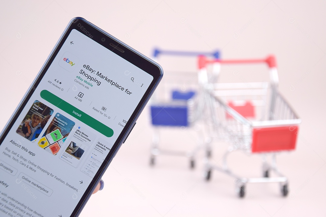 Carrinho de compras com um smartphone abriu o aplicativo Ebay na tela em um fundo rosa