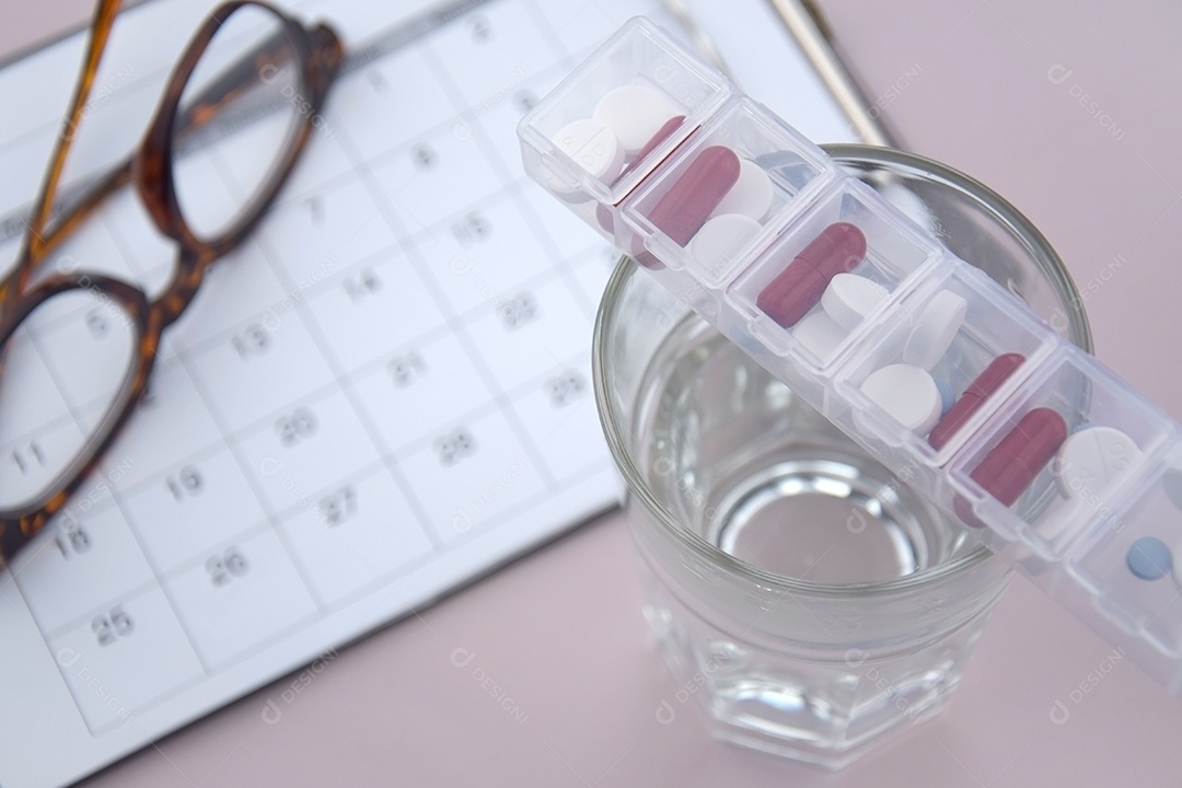 Copo com porta remédios em cima e calendário de fundo