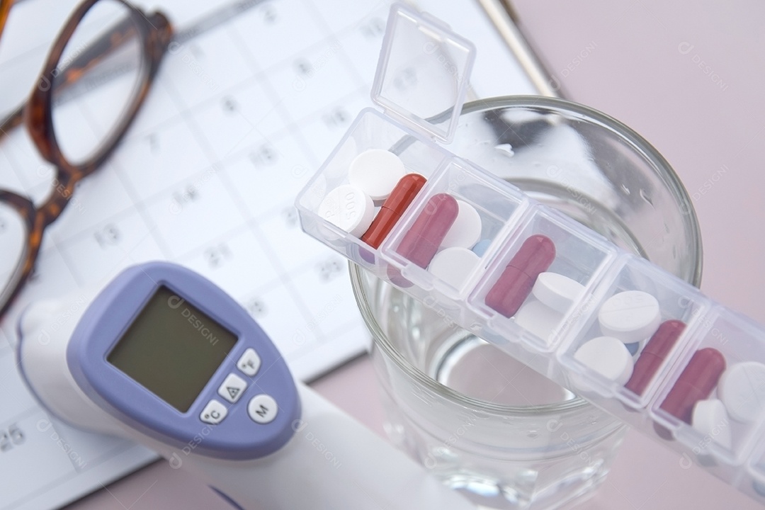 Copo com porta remédios em cima e calendário termômetro em fundo claro