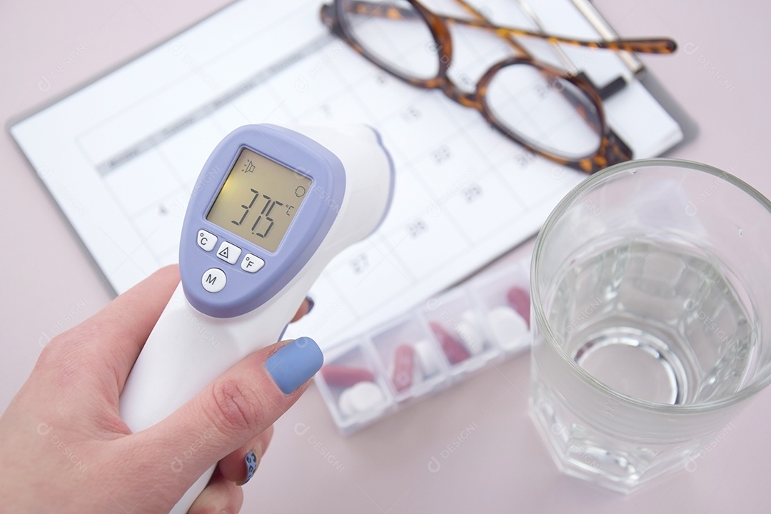 Mão feminina segurando termômetro copo óculos sobre fundo claro