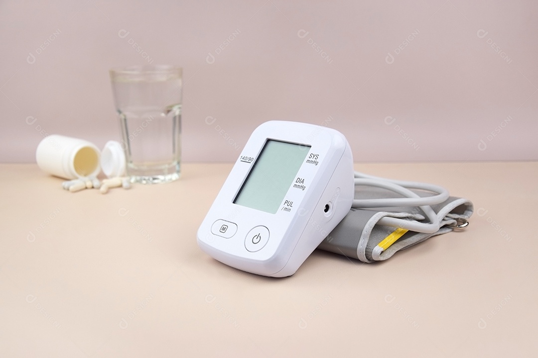 Aparelho digital de pressão arterial copo e comprimidos em um fundo claro